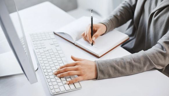 A woman at a computer taking notes in a notepad